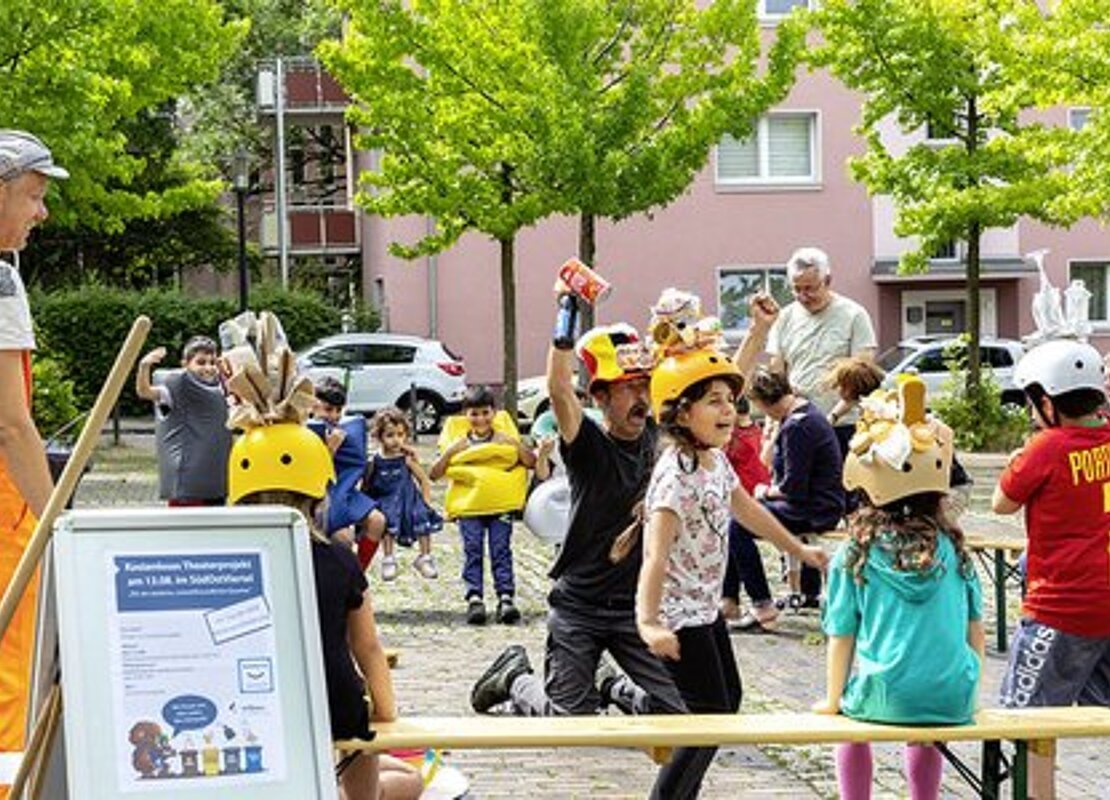 Kinder und Erwachsene auf einem Platz vor einem Wohngebäude bei einem Mitmach-Theaterstück 