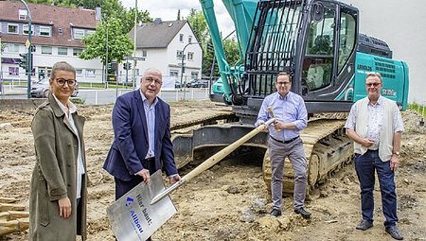Vier Personen mit Riesenspaten vor Raupenfahrzeug auf einem Baugelände – erster Spatenstich für ein Neubauvorhaben in der Matthias-Erzberger-Straße in Essen-Schonnebeck
