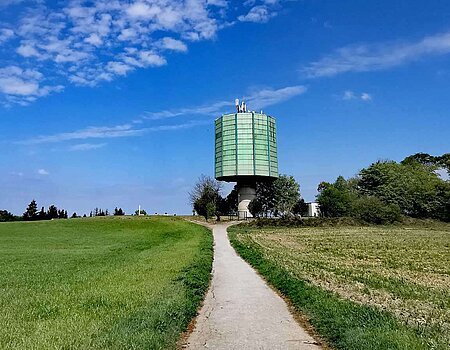 Grünes Feld mit Weg, der auf einen Wasserturm zuläuft