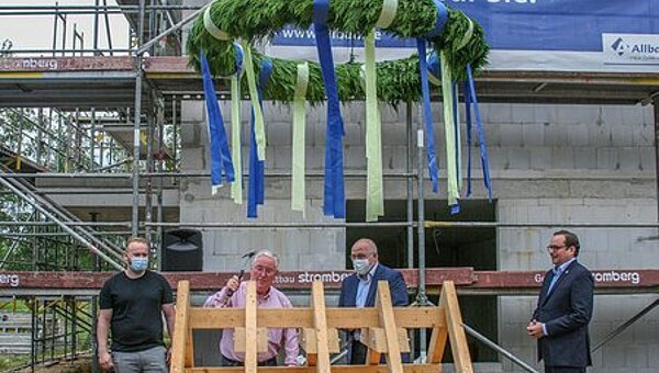 Vier Personen vor einem Baugerüst unter einem großen Richtkranz – Richtfest des Bauträgerprojektes ParkSide auf der Dilldorfer Höhe in Essen